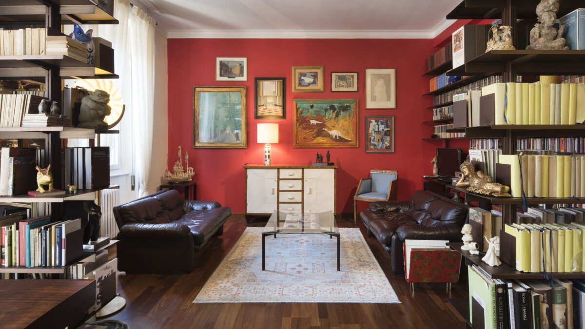 sala-con-tavolo-di-vetro-piastrelle-gio-ponti-design-gfr-librerie-e-quadri-con-parete-rossa